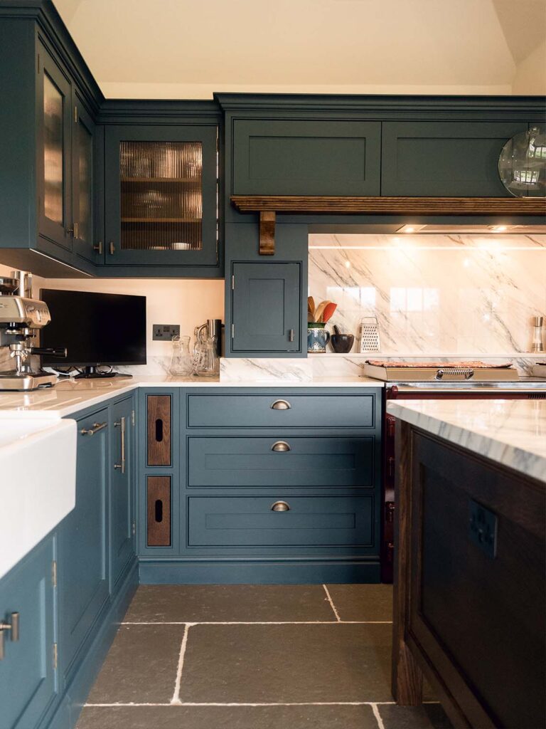 A view of a traditional green shaker-style kitchen island. The island features a light wood countertop, a deep sink, and classic detailing, all contributing to the timeless, bespoke design.