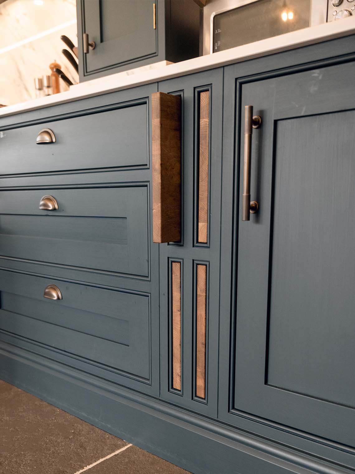 A close-up of a kitchen corner with an antique-style chair and green shaker-style cabinets. The image highlights the detailed, classic design and the warm, inviting atmosphere.
